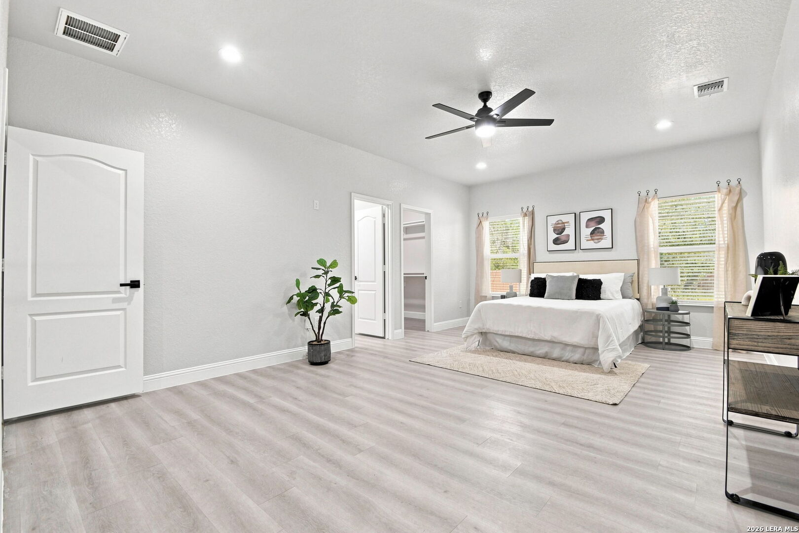 Staged bedroom with a ceiling fan, large windows, and light wood-look flooring.