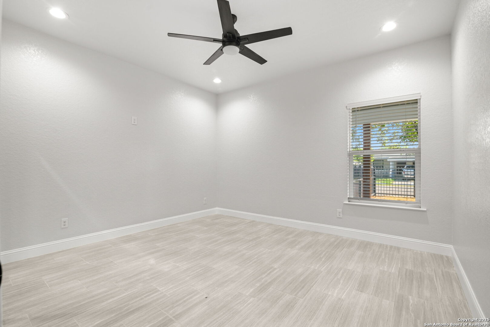 Empty room with light tile flooring, a black ceiling fan, and a window with blinds.