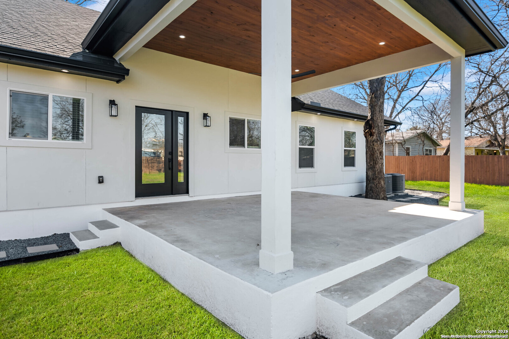 Covered concrete patio with a wood-plank ceiling, white columns, and black-framed doors.