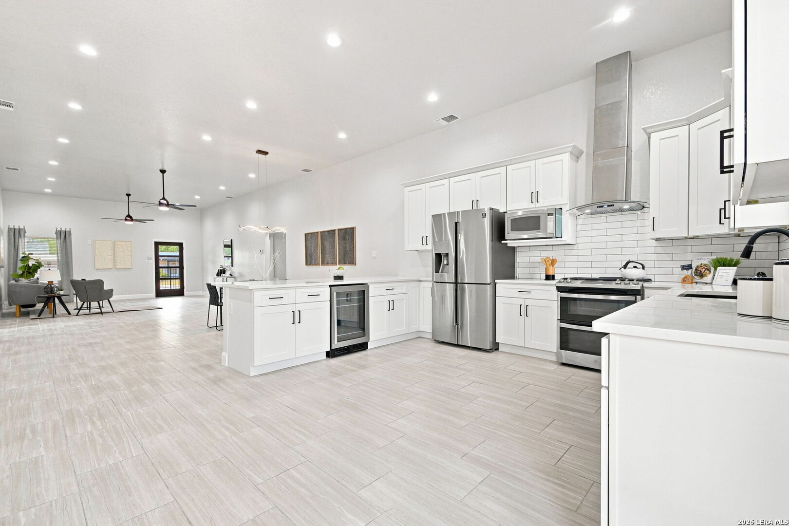 Bright open kitchen with white cabinetry, stainless steel appliances, and an island beside the living area.