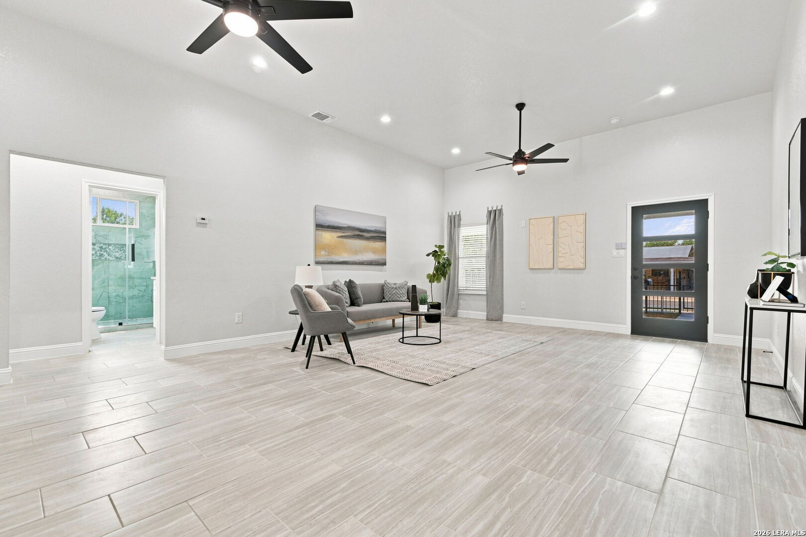 Staged living room with a high ceiling, ceiling fans, pale tile floors, and a glass-panel exterior door.
