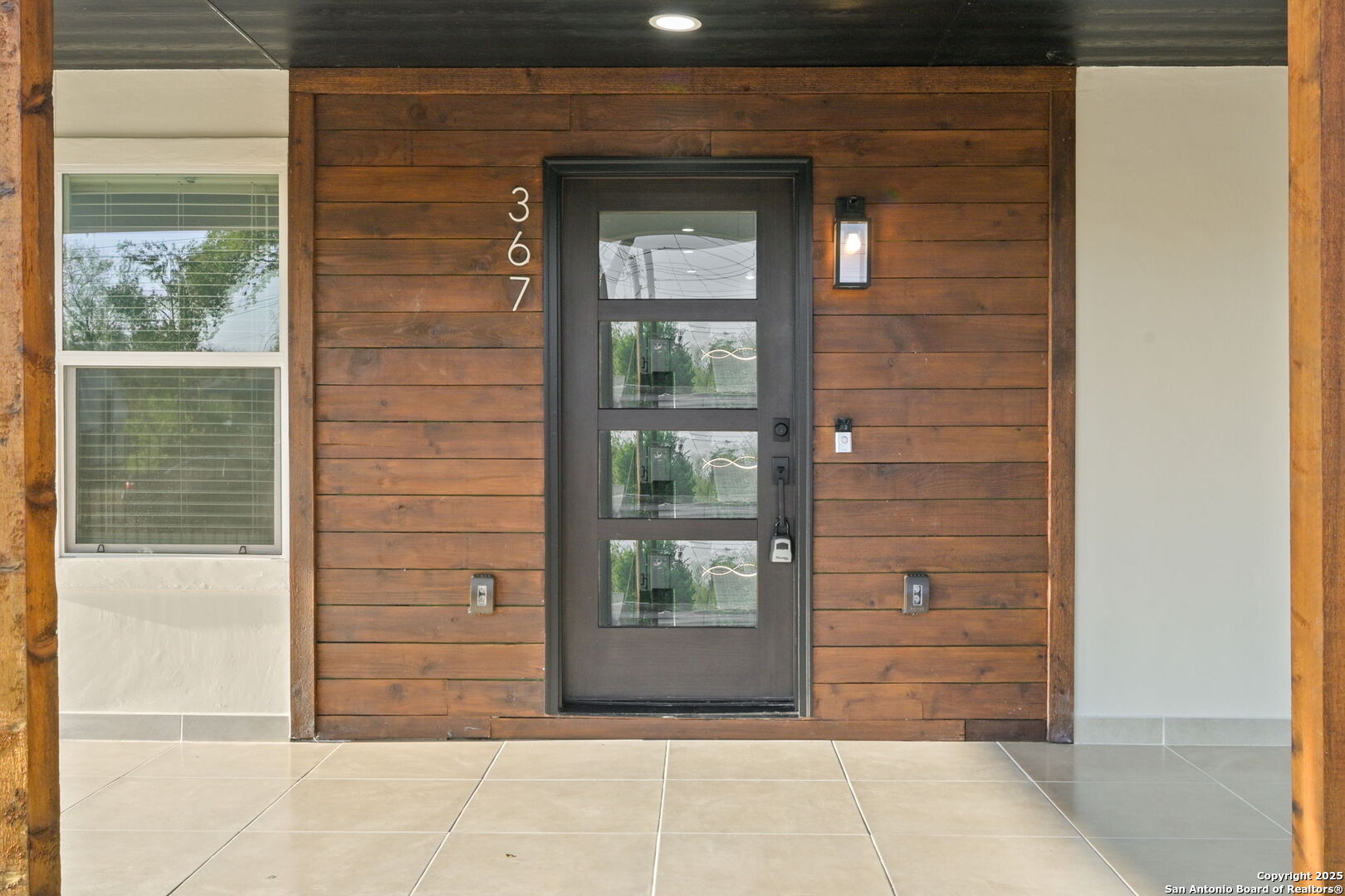 Front entry with a dark glass-paneled door, warm wood siding, and a tiled porch.