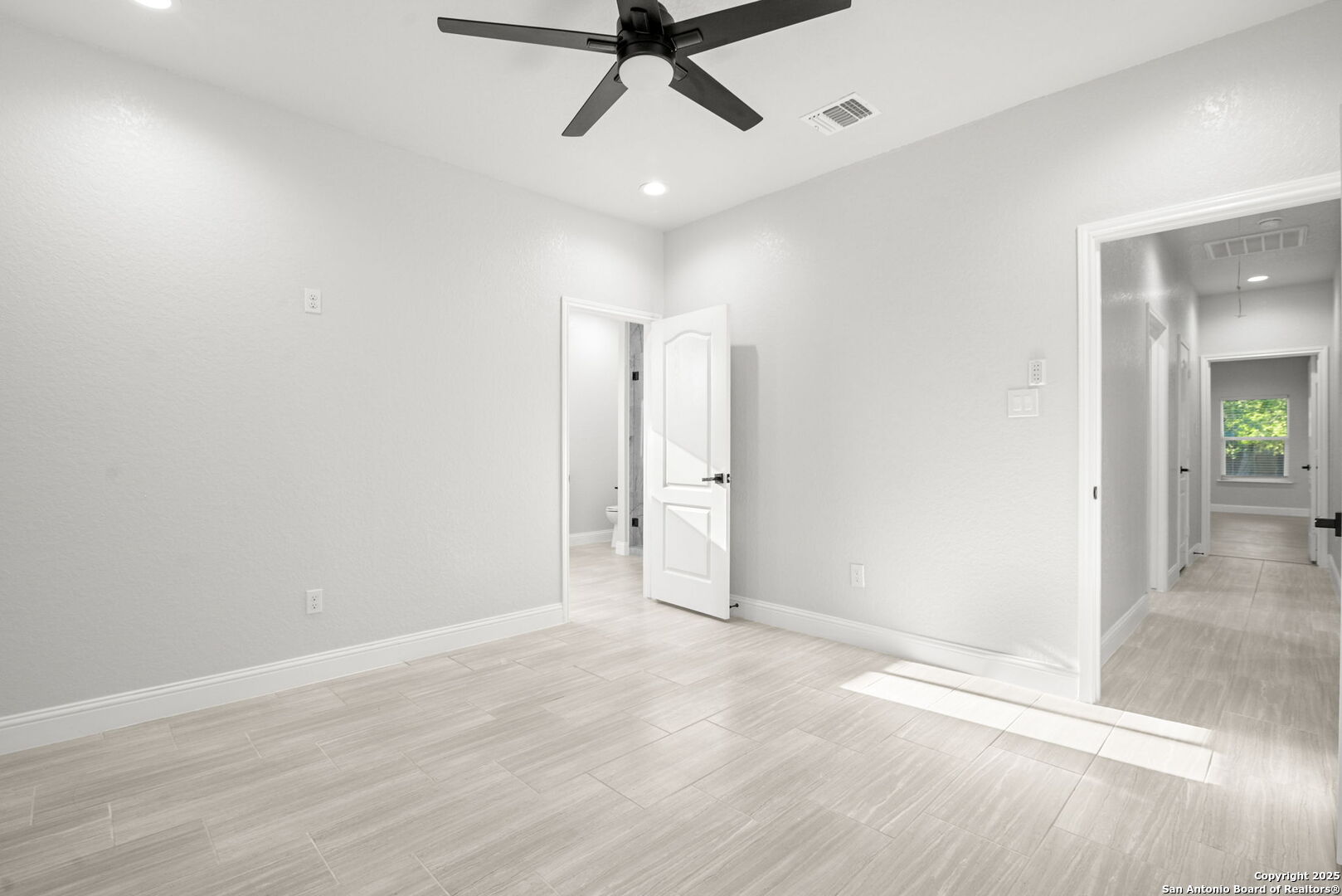 Empty room with light tile flooring, a black ceiling fan, and open doorways.