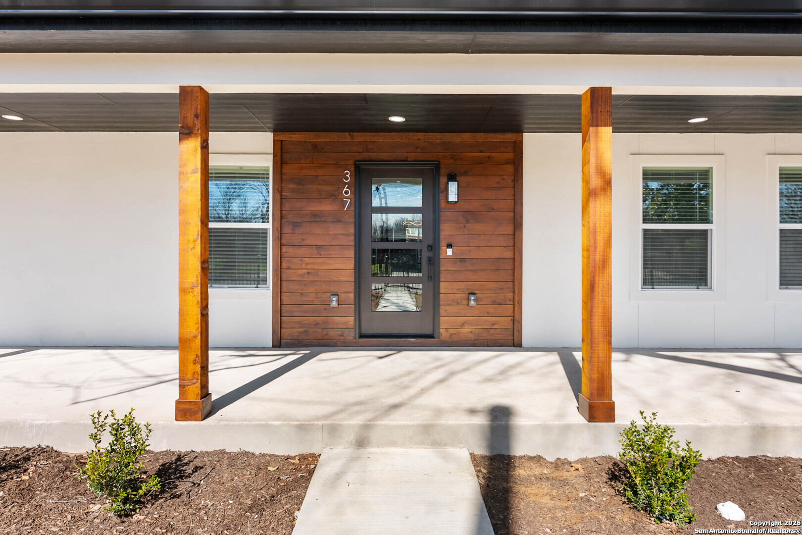 Home entrance with a dark glass door set in a wood-paneled facade beneath a covered porch.