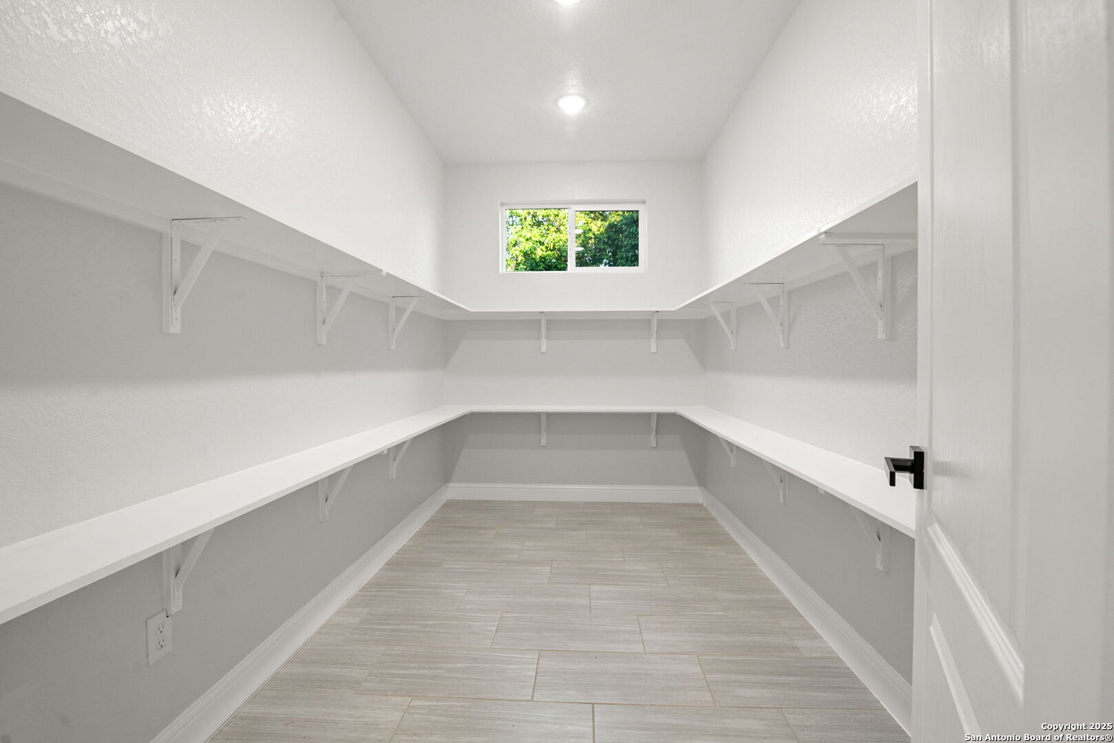 Walk-in pantry with white wraparound shelves, tile flooring, and a high window.