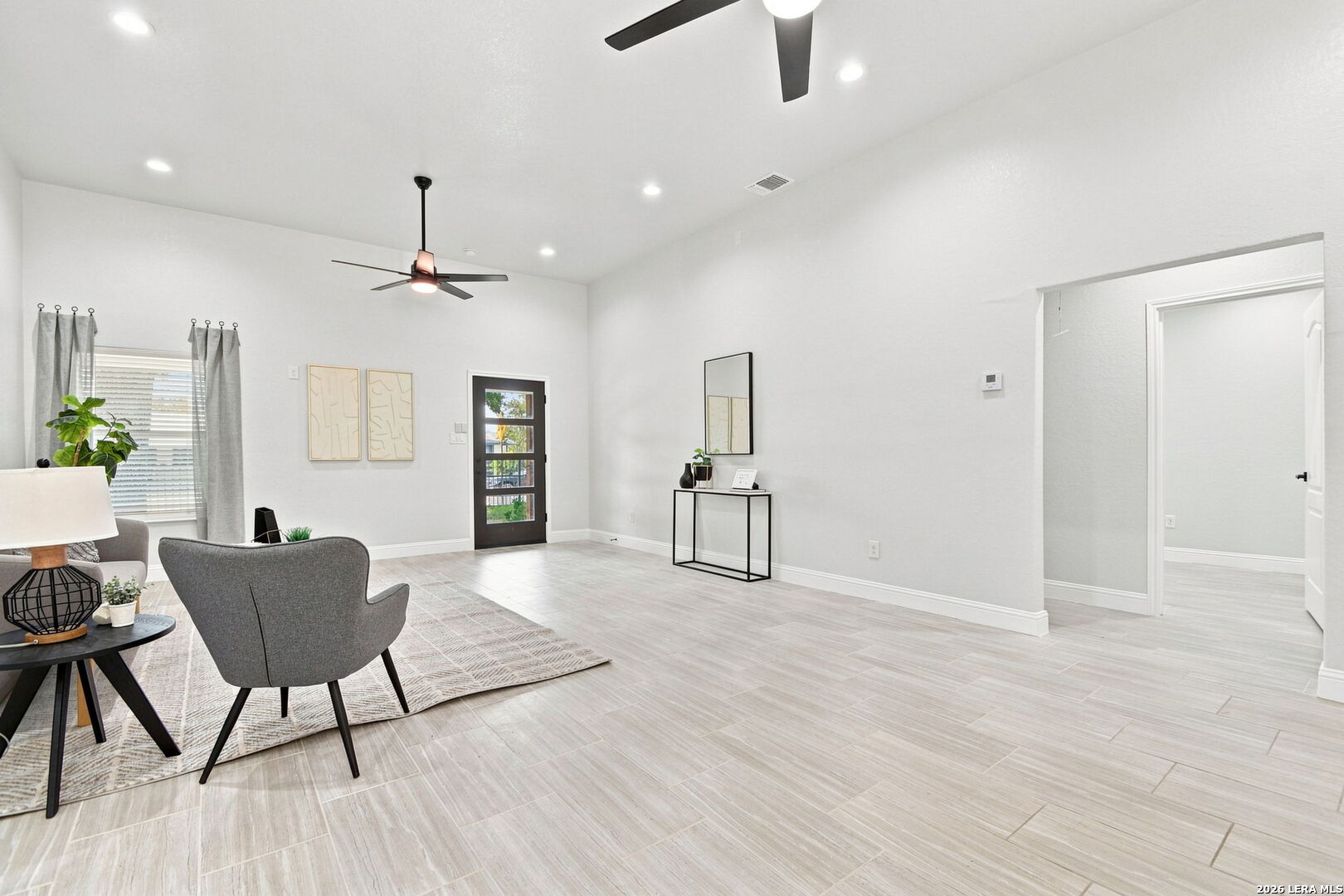 Staged living room with gray seating, pale tile floors, and a black-framed glass door.