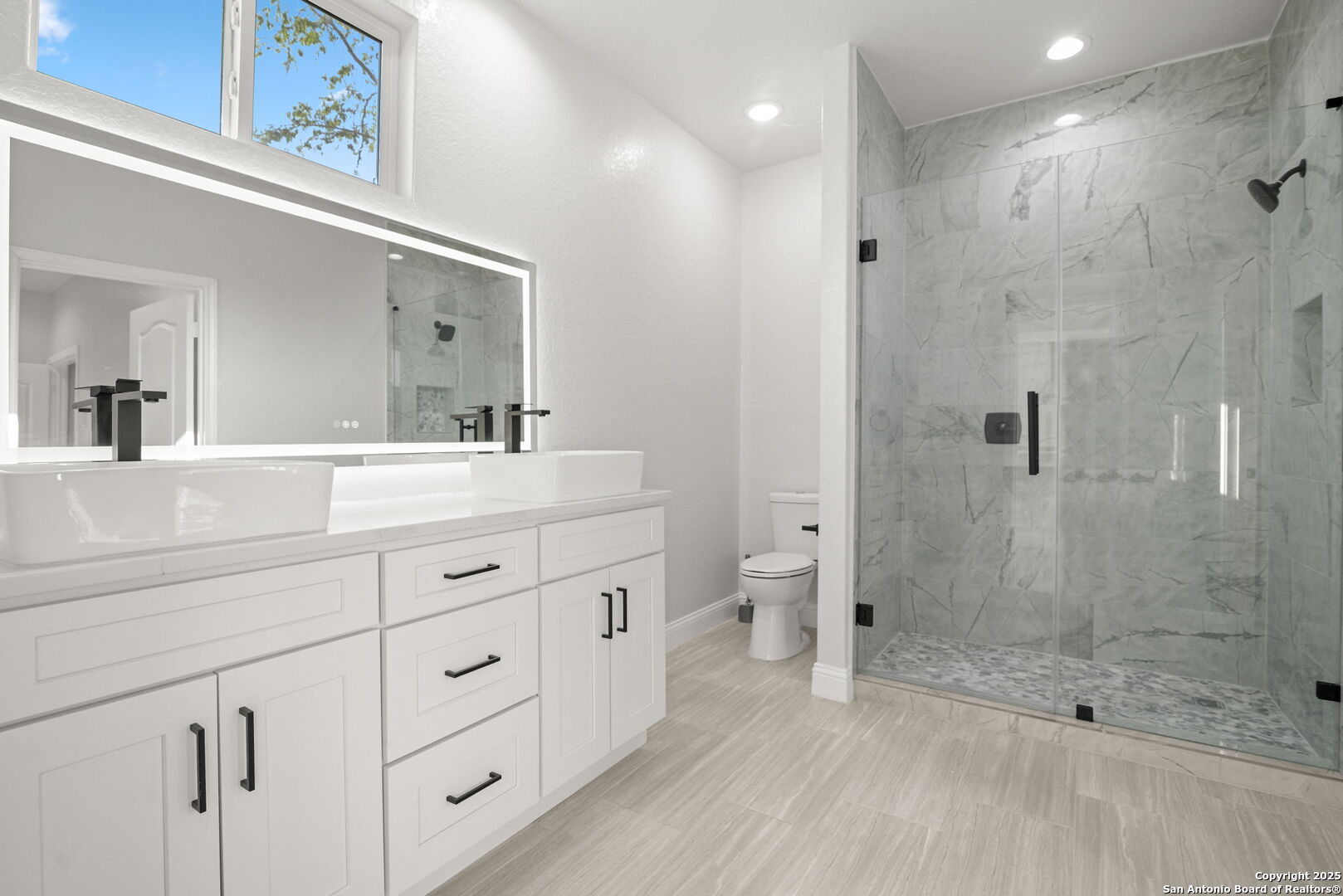 Bathroom with a double-sink vanity, large mirror, and glass-enclosed marble-look shower.
