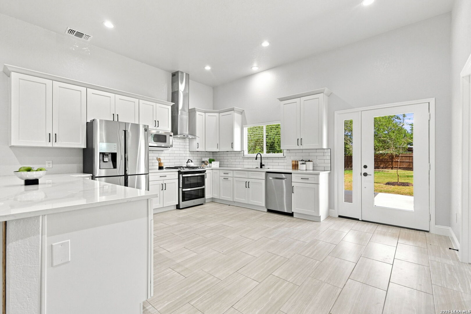 Bright kitchen with white cabinetry, stainless steel appliances, tile floors, and French doors to the yard.