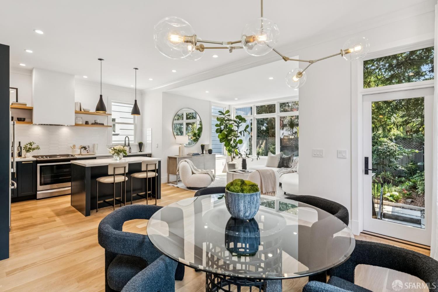 Open-plan kitchen and dining area with a black island, glass table, and leafy garden views.