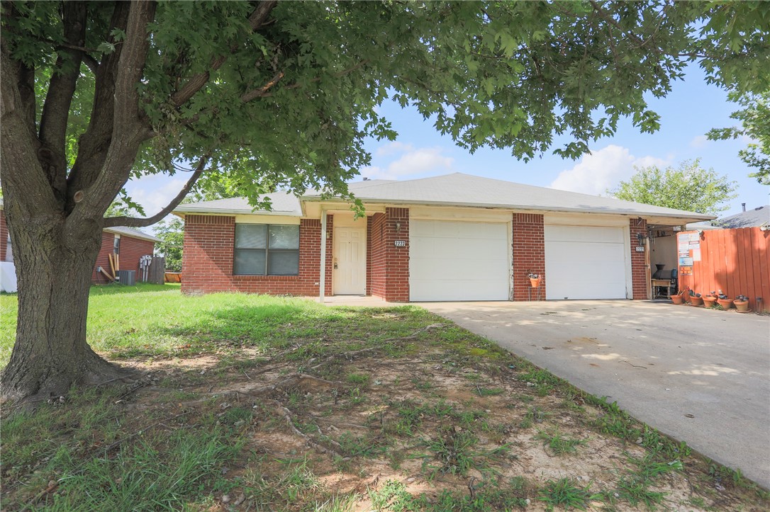 Single-story brick home with two garage doors, a wide driveway, and a large shade tree.