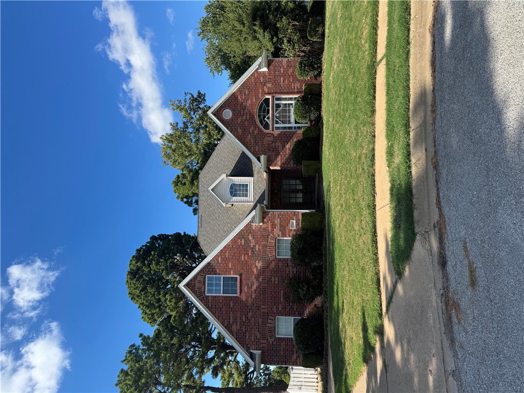 Red brick house with multiple gables and an arched window, fronted by a green lawn.