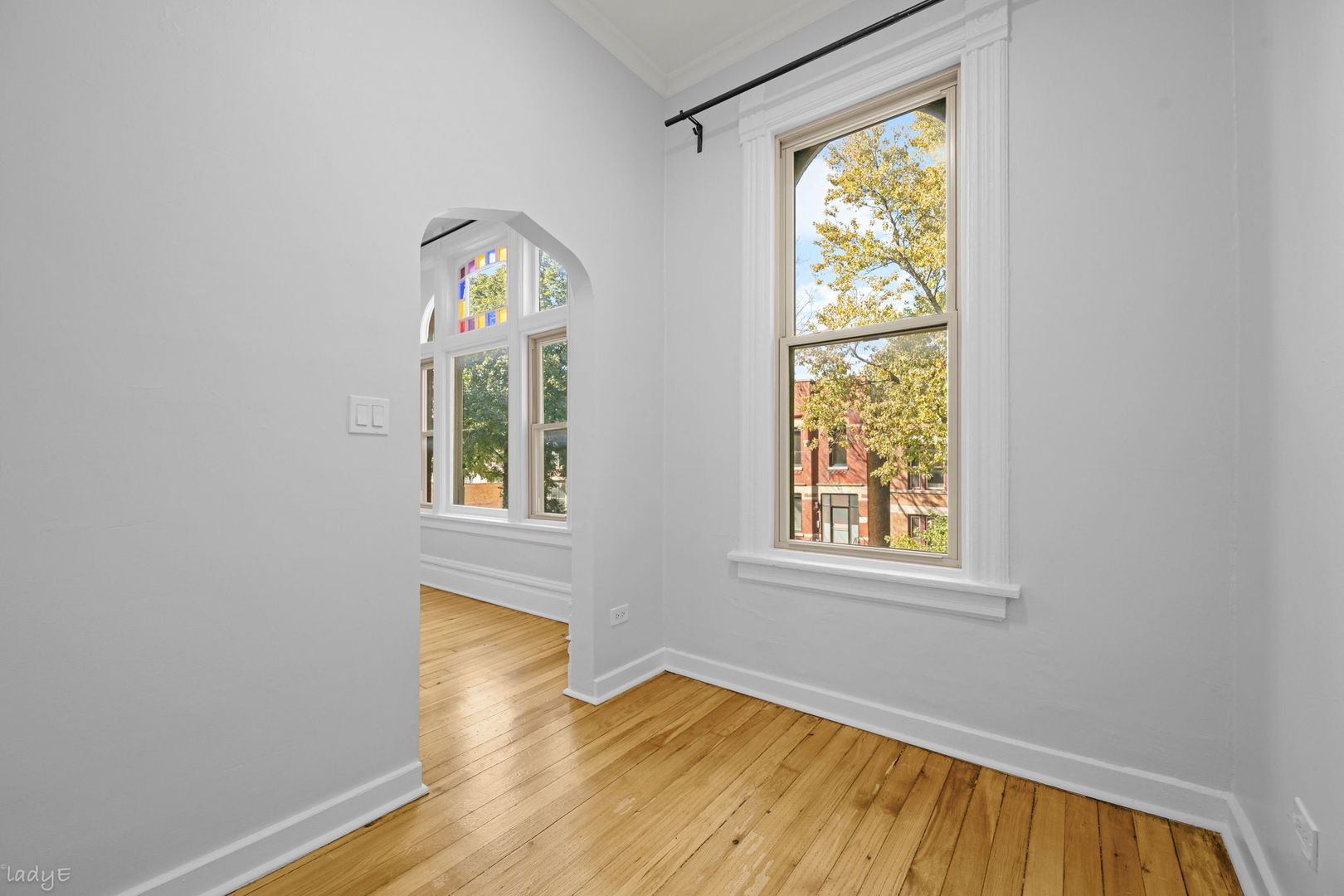 Empty room with hardwood floors, tall windows, and a stained-glass transom.