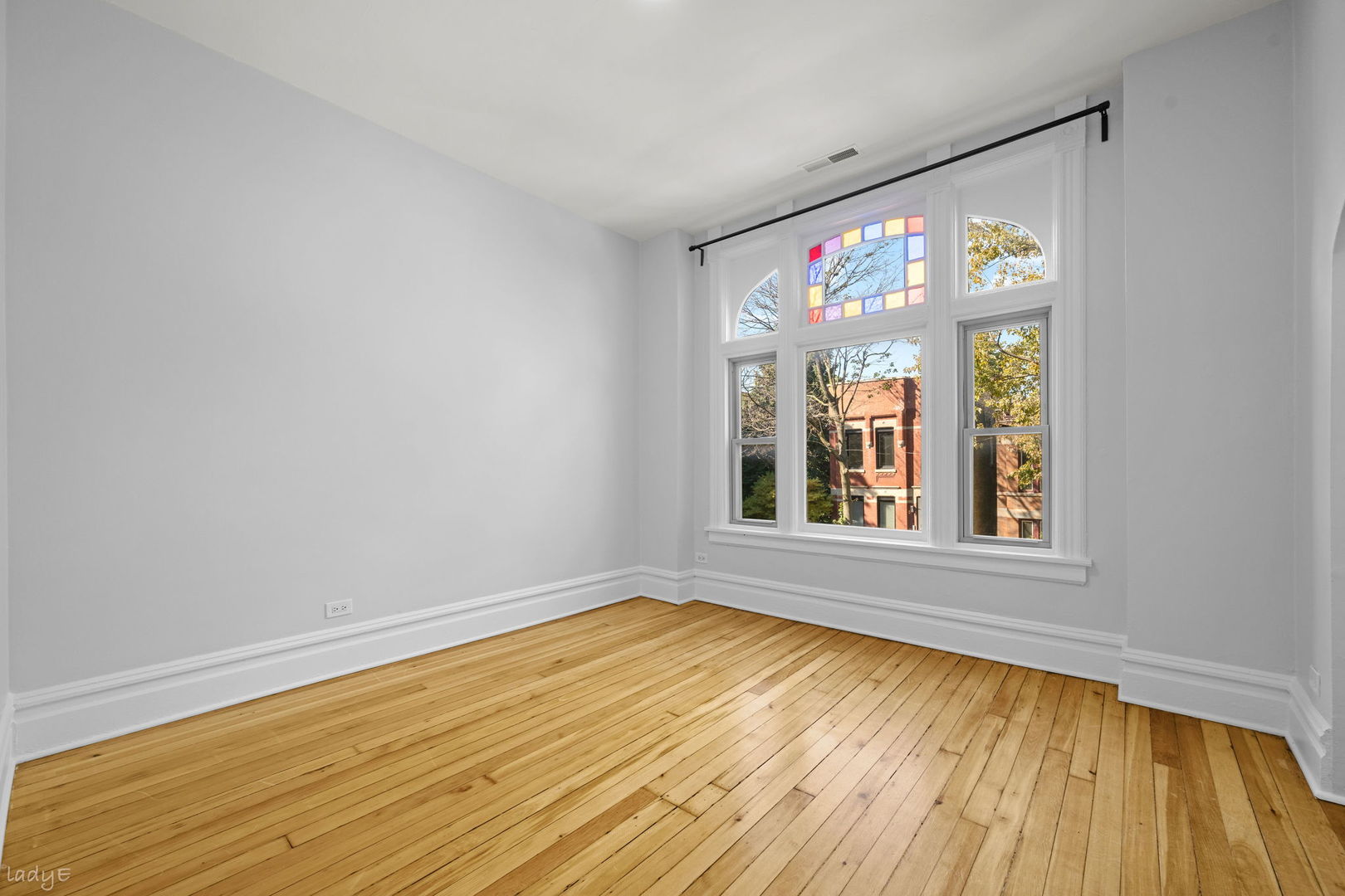 Vacant room with hardwood floors and a large window featuring colored glass panes.
