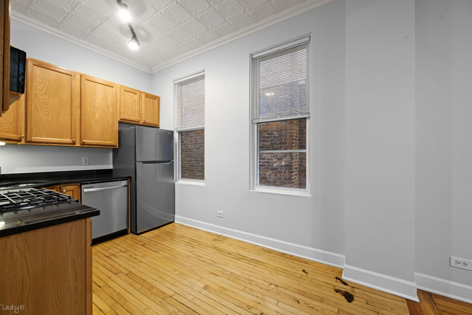 Kitchen with oak cabinets, stainless steel appliances, hardwood floors, and tall windows facing a brick wall.