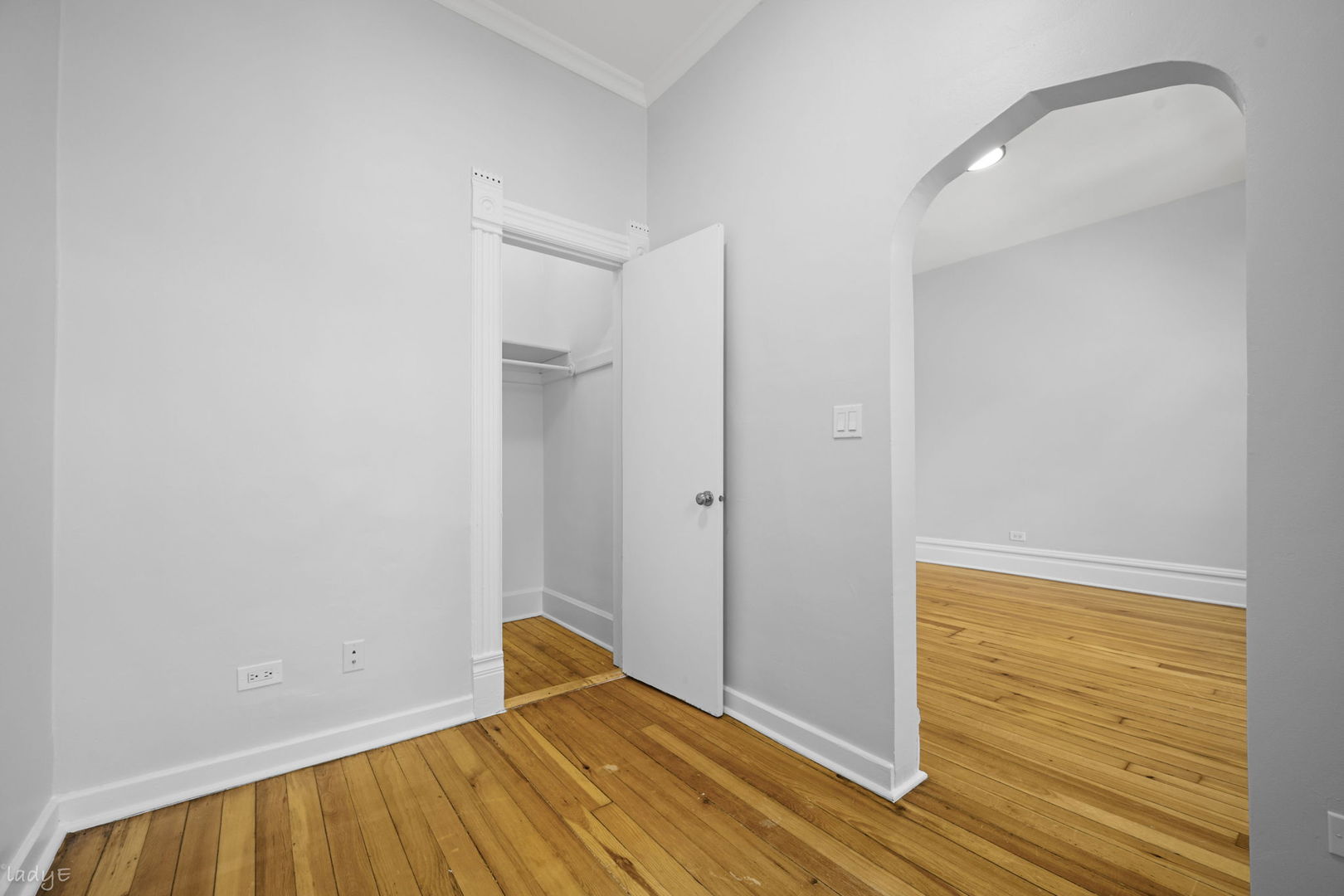 Unfurnished apartment interior with hardwood floors, an open closet, and an arched doorway.