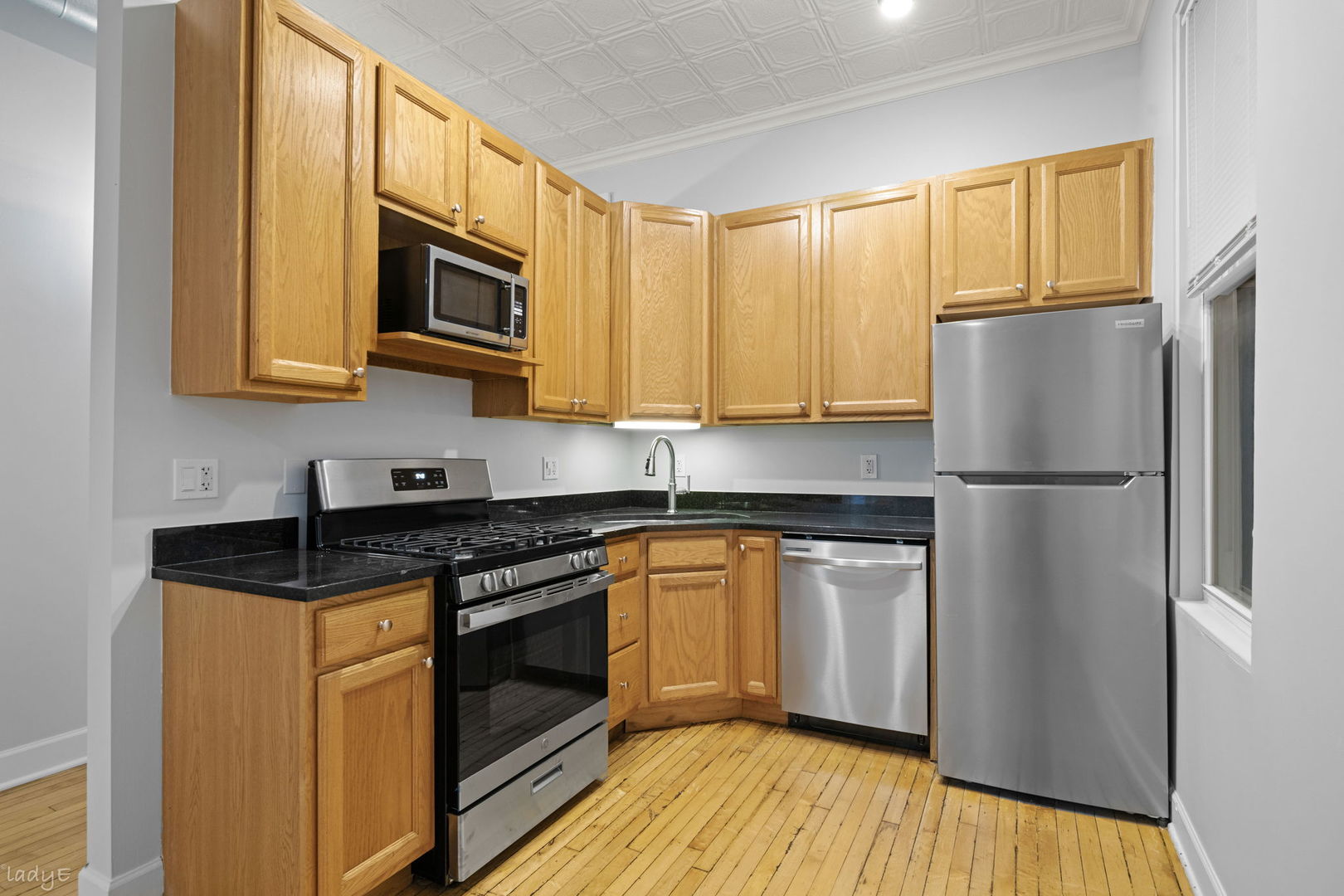 Kitchen with oak cabinets, black countertops, stainless steel appliances, and hardwood floors.