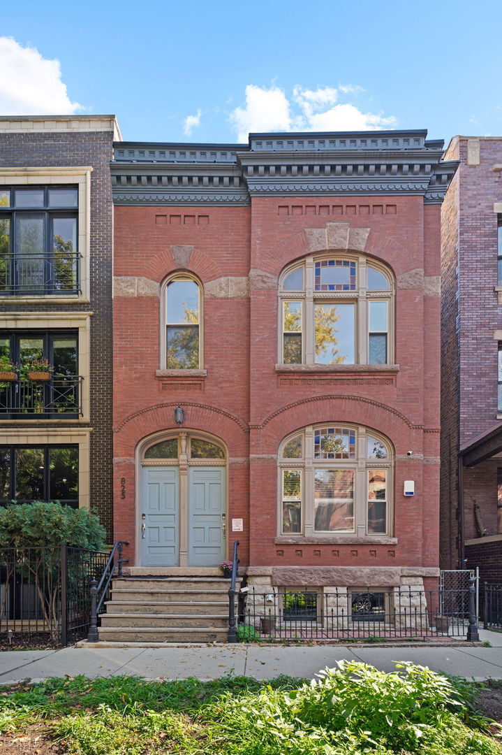 Red-brick West Town residence with ornate stone trim, arched windows, and pale blue entry doors.