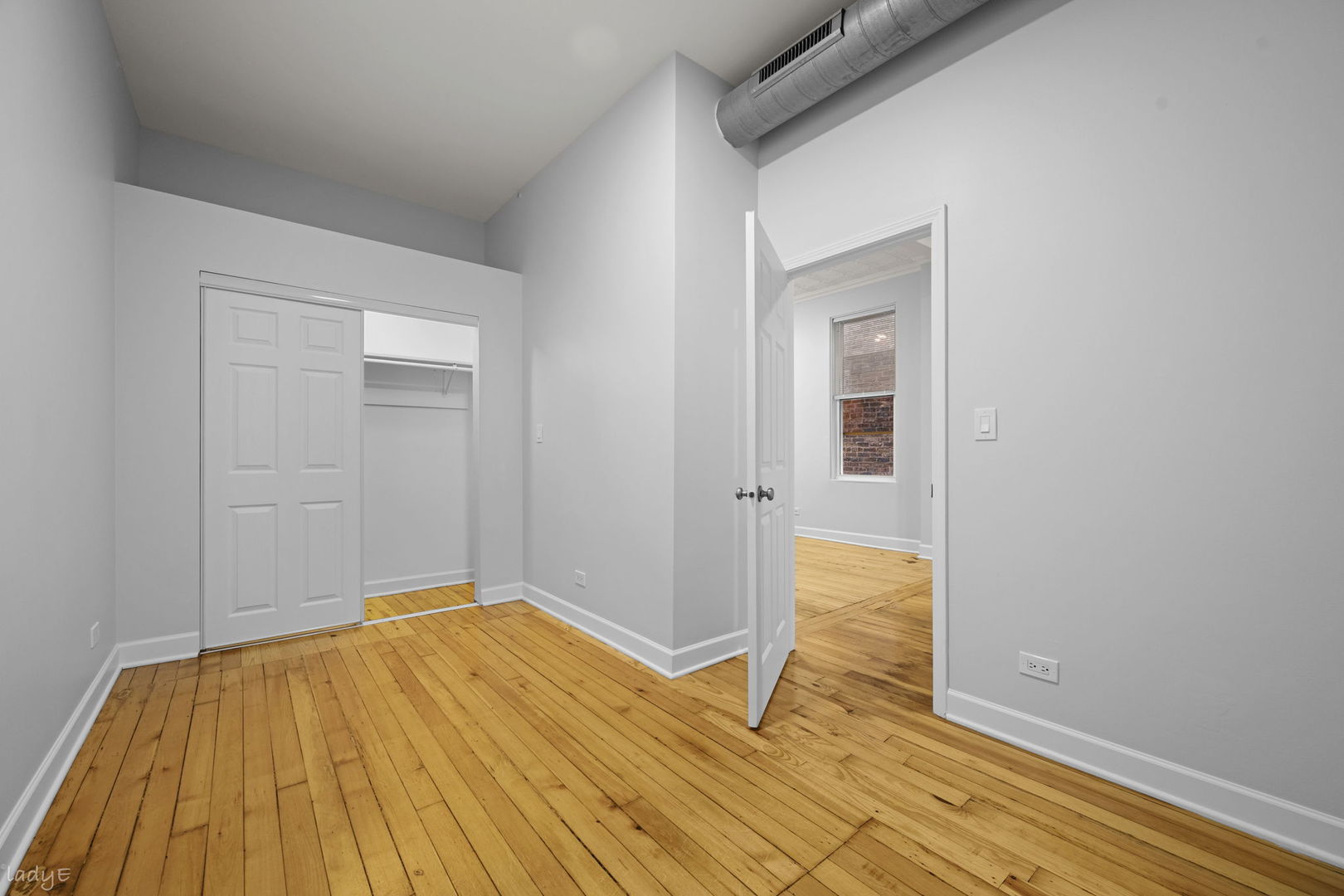 Empty bedroom with hardwood floors, a closet, high ceilings, and exposed ductwork.