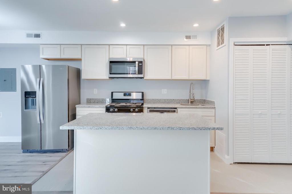 Kitchen with white cabinets, stainless appliances, and a large granite island.
