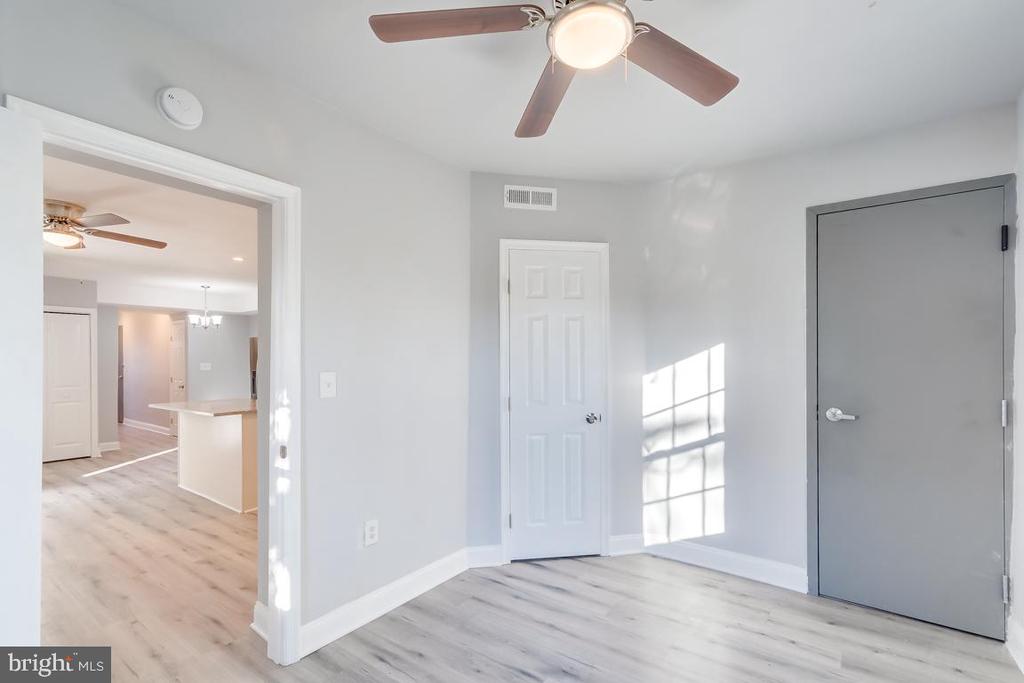 Vacant room with light wood-look flooring, a ceiling fan, and sunlight across the wall.