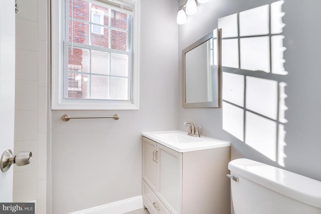 Bright bathroom with a white vanity, bathtub, and sunlight streaming through a large window.