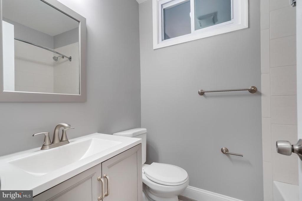 Bathroom with a white vanity, toilet, large mirror, and small high window.