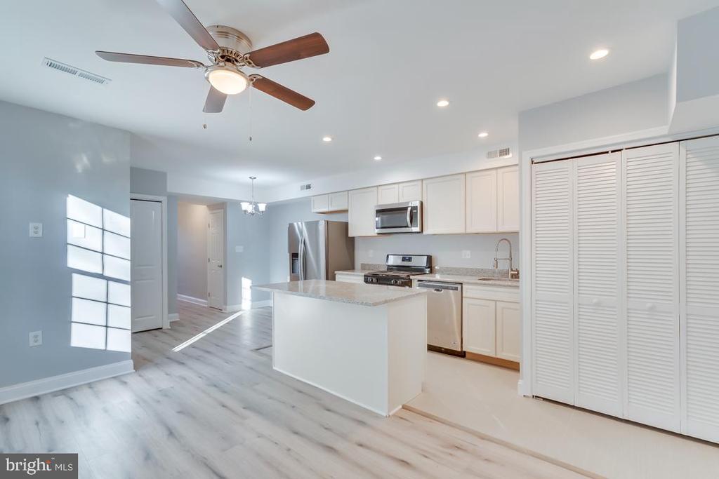 Open kitchen with white cabinets, stainless steel appliances, a central island, and gray wood-look flooring.