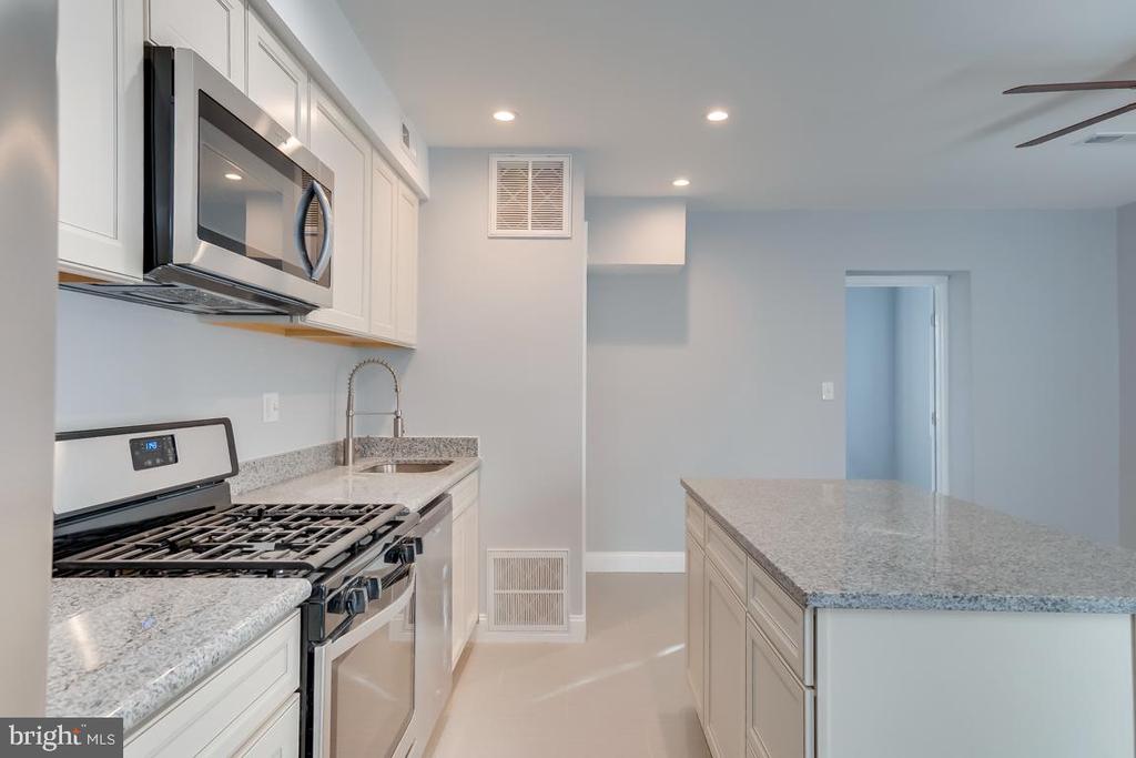 Kitchen with a large granite island, white cabinets, and stainless steel gas range.