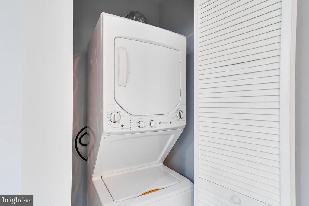 Stacked white washer and dryer in a laundry closet beside a louvered door.