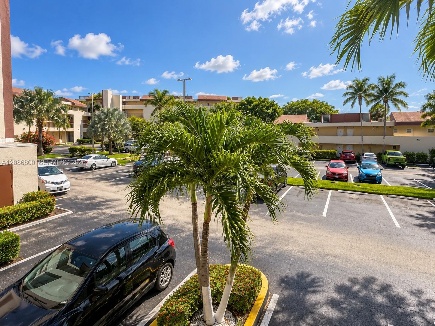 Condominium parking lot with palm trees, parked cars, and low-rise buildings.