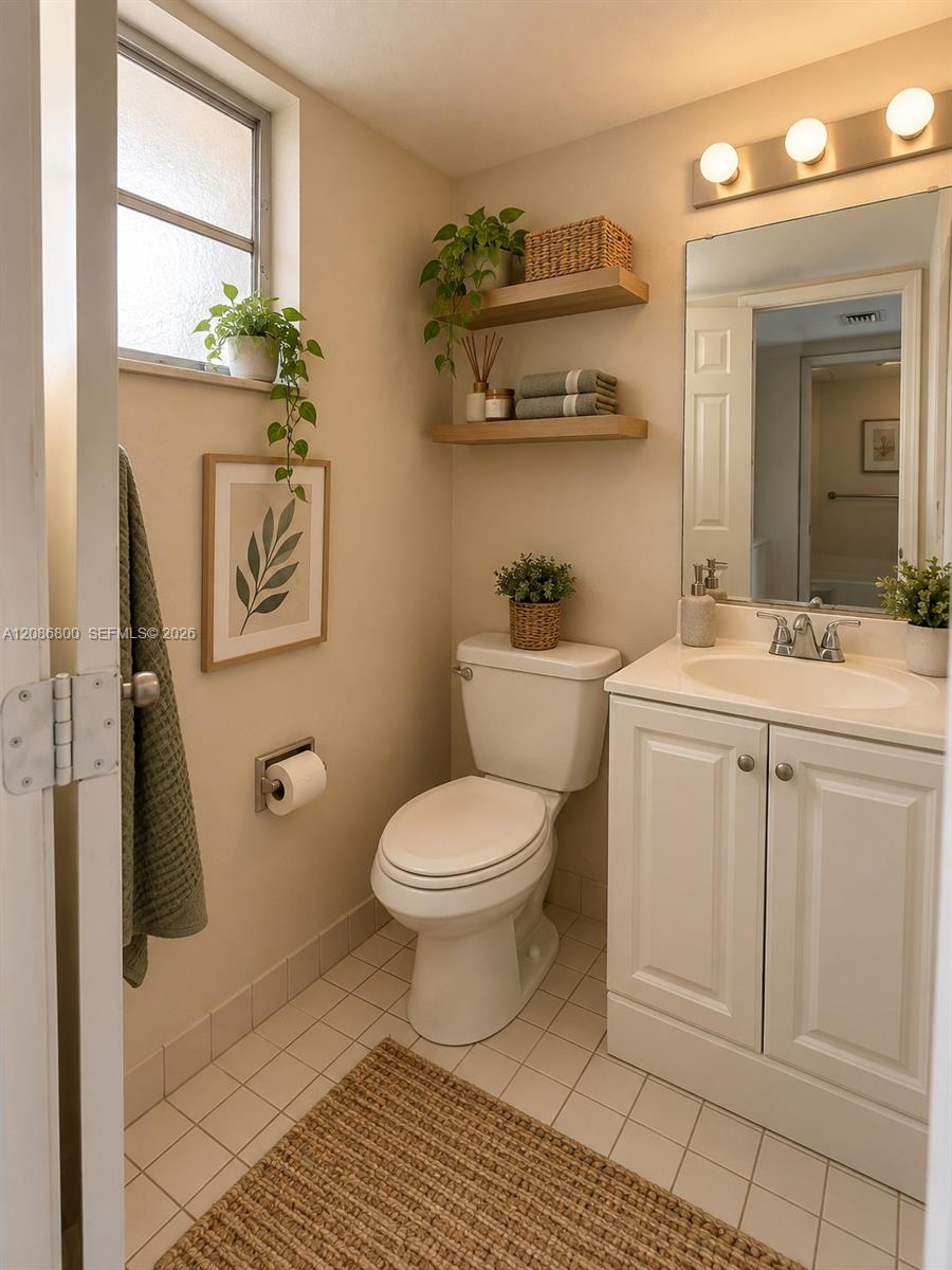 Bathroom with a white vanity and toilet, tiled floor, and floating shelves with plants and towels.