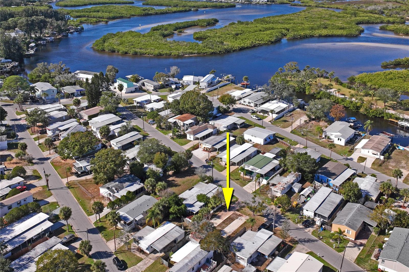 Aerial view of homes beside winding waterways, with a yellow arrow marking a neighborhood parcel.