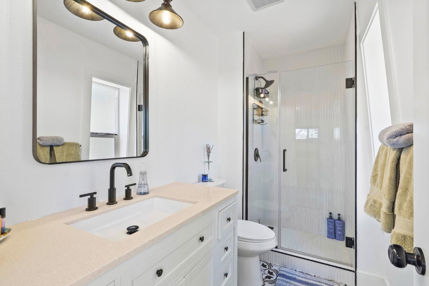 Bathroom with a white vanity, black fixtures, and a glass-enclosed shower with patterned floor tile.
