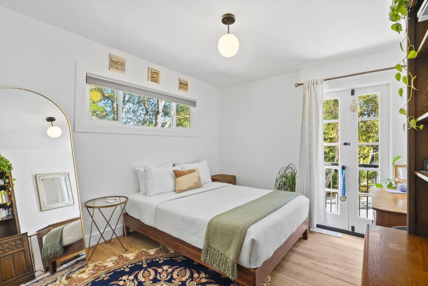 Bright bedroom with a white bed, patterned rug, and French doors opening to greenery.