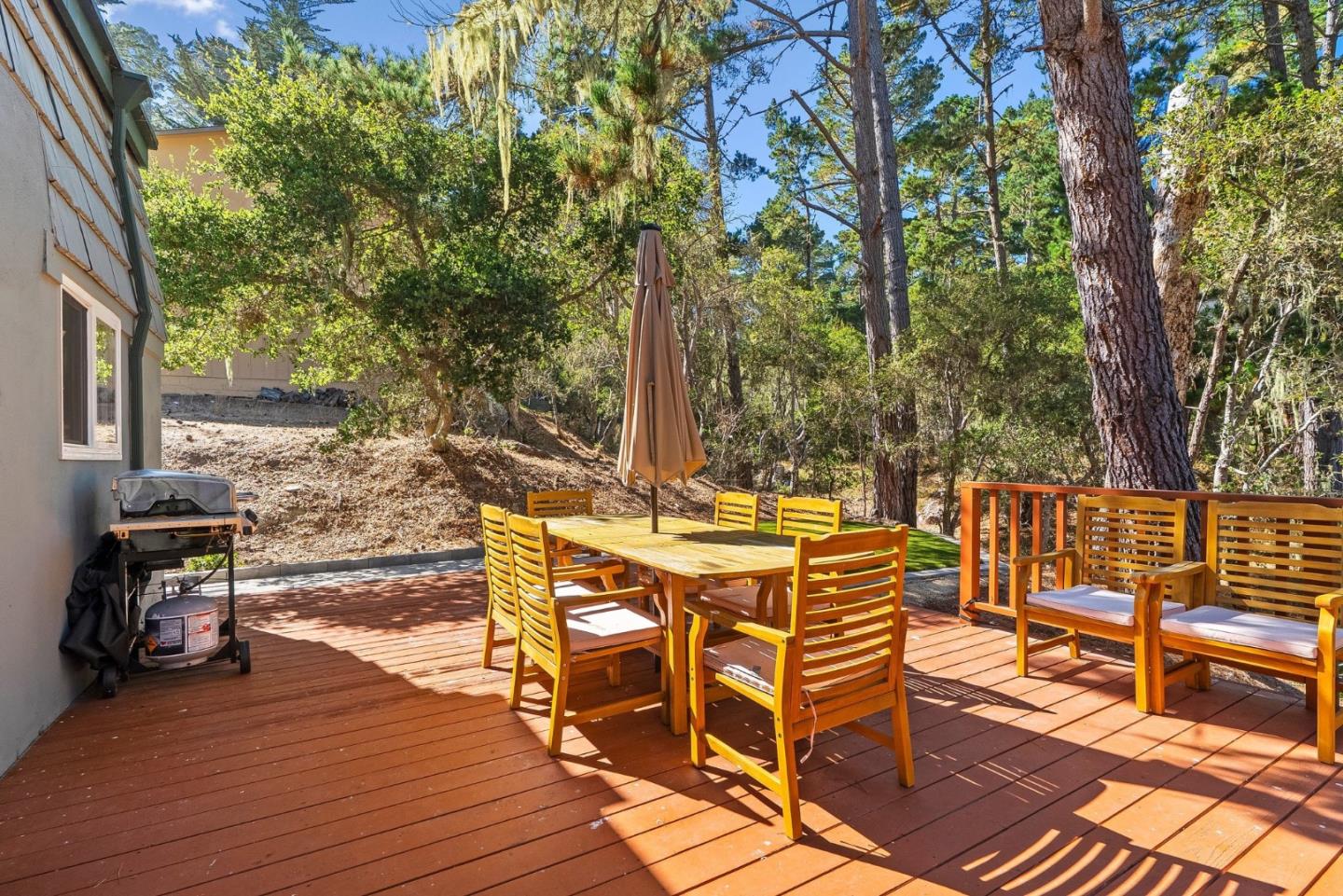 Wooden deck with outdoor dining set and grill, surrounded by tall trees.