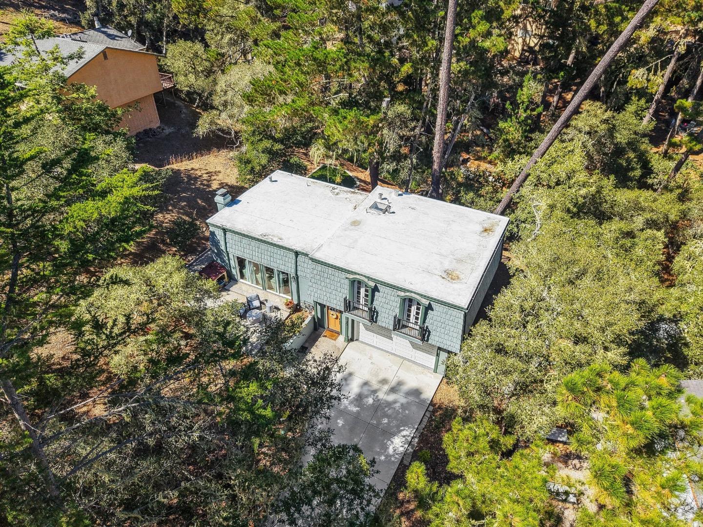 Aerial view of a gray-green house nestled among trees, with a driveway and small patio.
