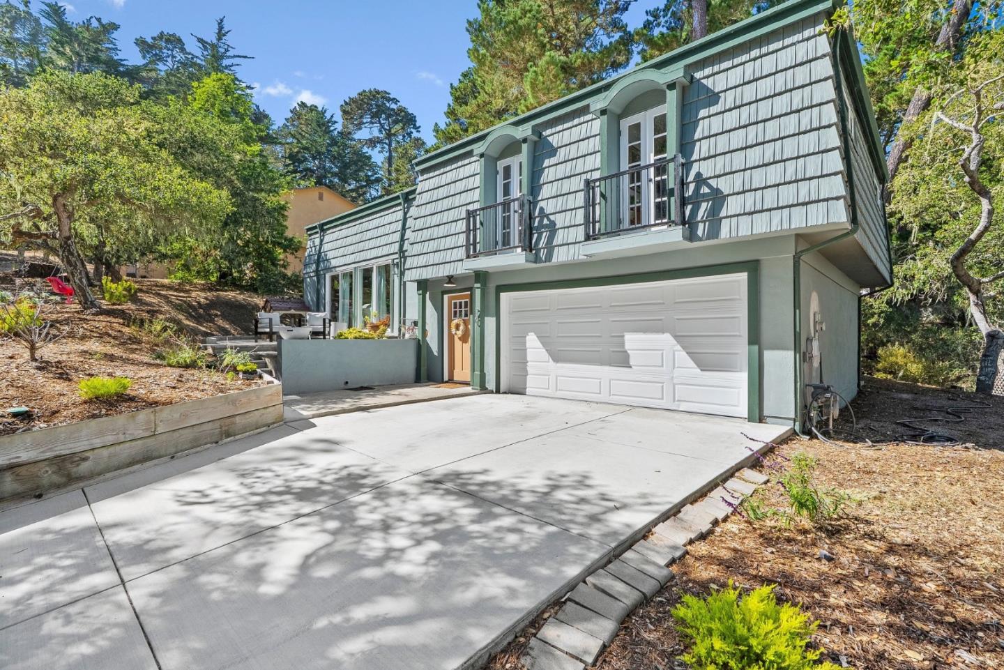 Gray-green shingle-sided house with two small balconies above a double garage and broad concrete driveway.