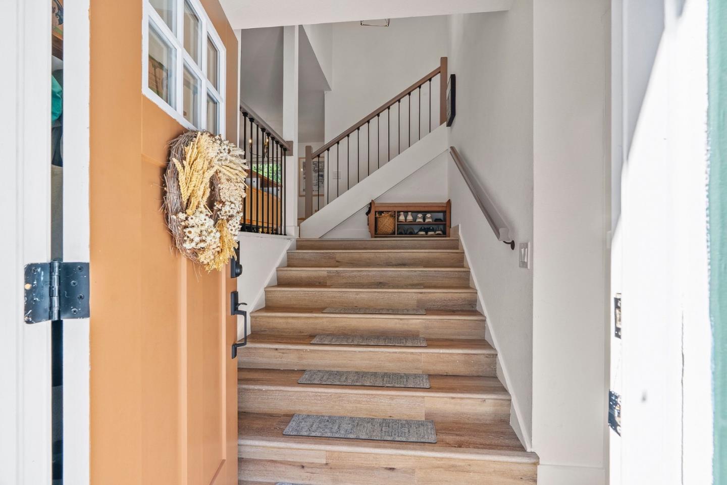 Entryway staircase with wood steps, black railings, and an open front door with a dried wreath.