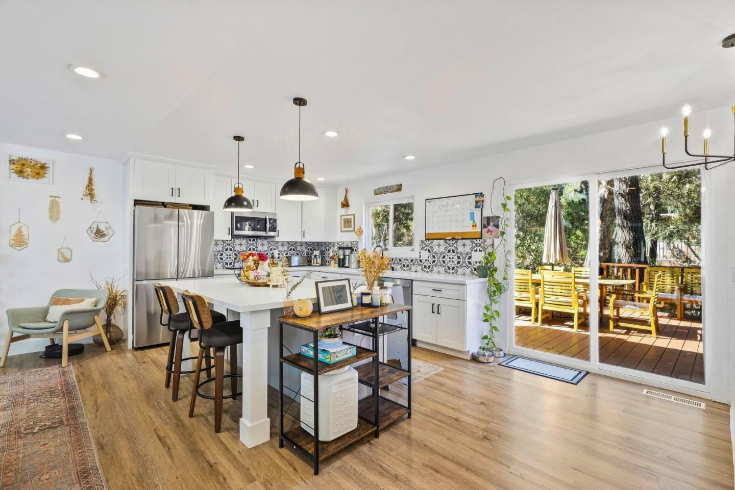 Bright kitchen with a large island, patterned tile backsplash, and sliding doors to a tree-shaded deck.