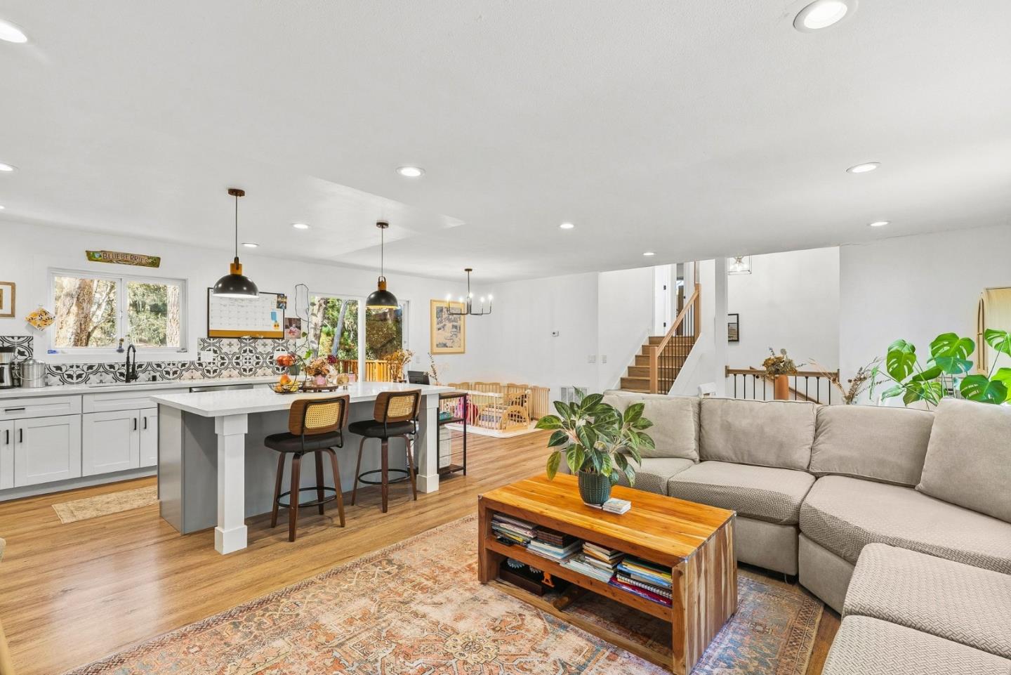 Open-plan kitchen and living room with a large island, patterned backsplash, wood floors, and staircase.