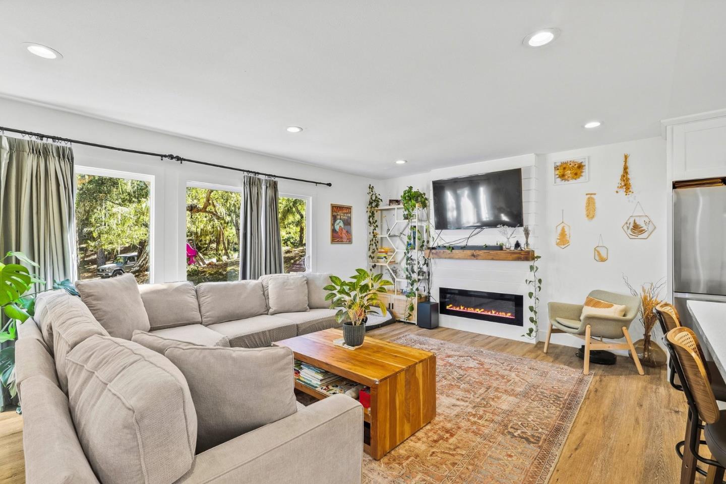 Living room with a large sectional sofa, electric fireplace, and broad windows overlooking trees.