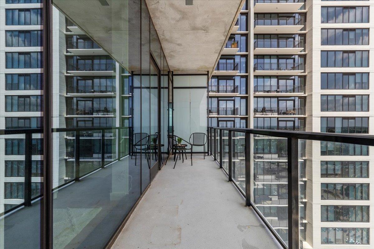 Condo balcony with glass railings, concrete flooring, and chairs facing neighboring high-rises.