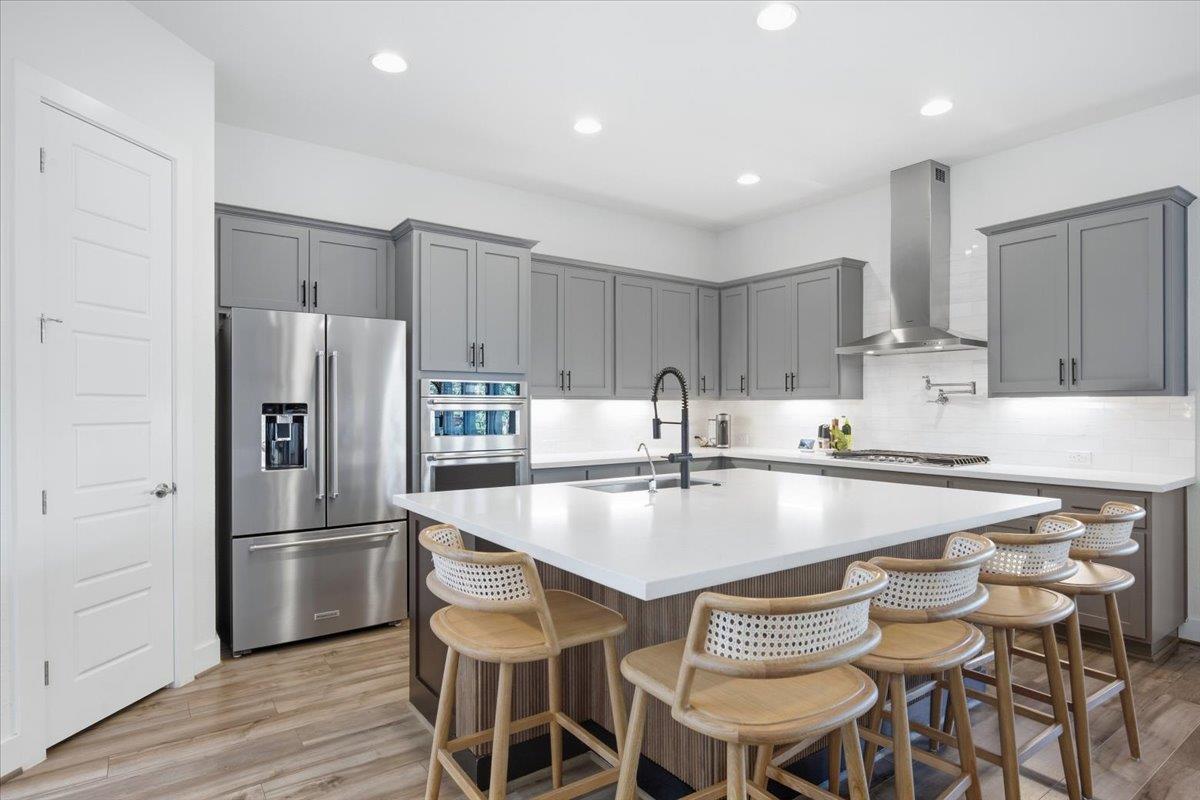 Modern kitchen with gray cabinets, stainless steel appliances, and a large island lined with bar stools.