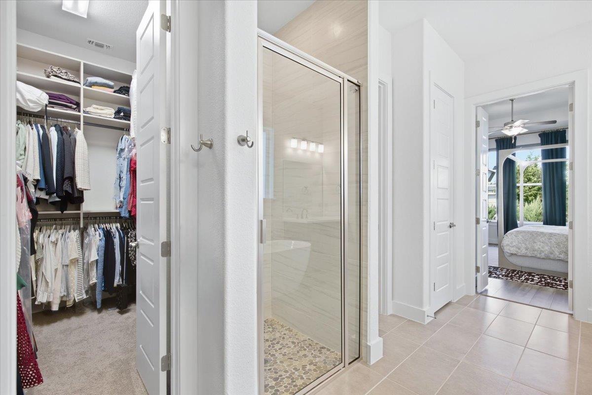 Bathroom with a glass shower and pebble floor, opening to a clothes closet and bedroom.