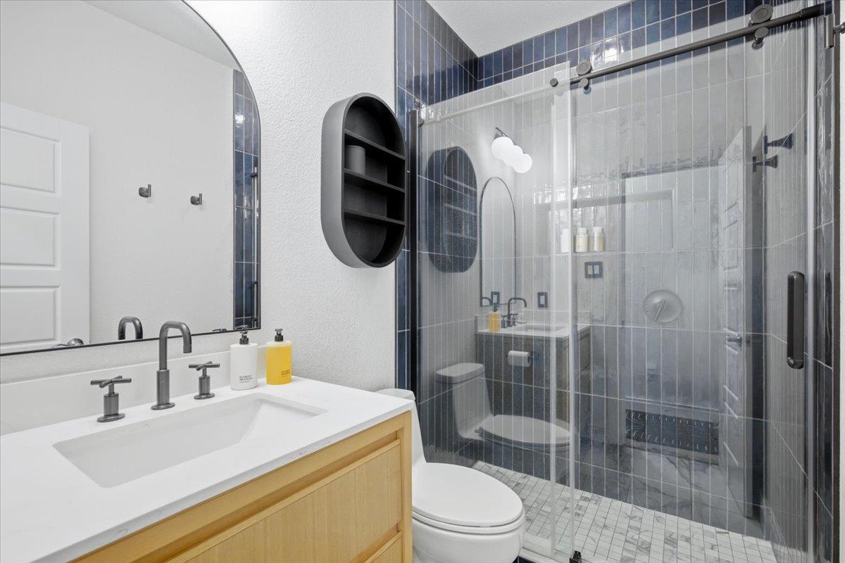 Bathroom with a light wood vanity and glass shower tiled in blue and gray.