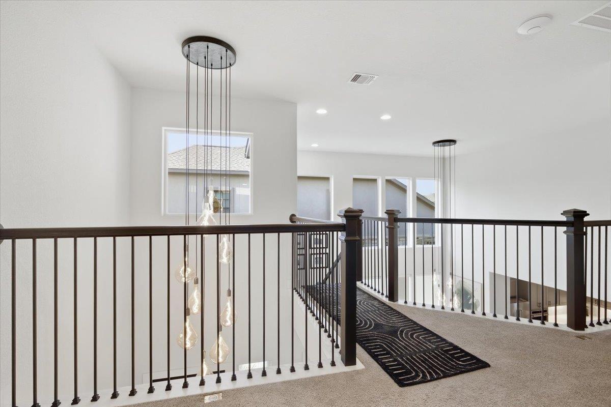 Upstairs landing overlooking a two-story foyer, with dark railings and cascading pendant lights.