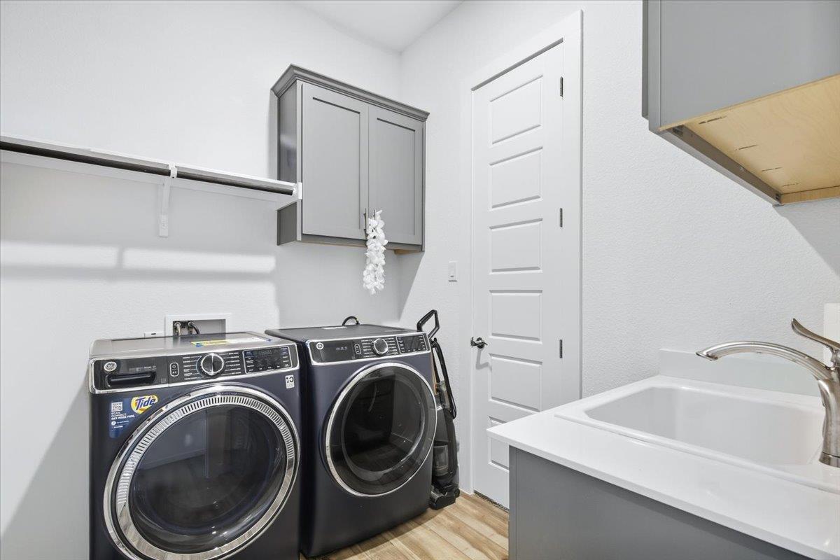 Laundry room with front-loading washer and dryer, a deep utility sink, and gray cabinetry.