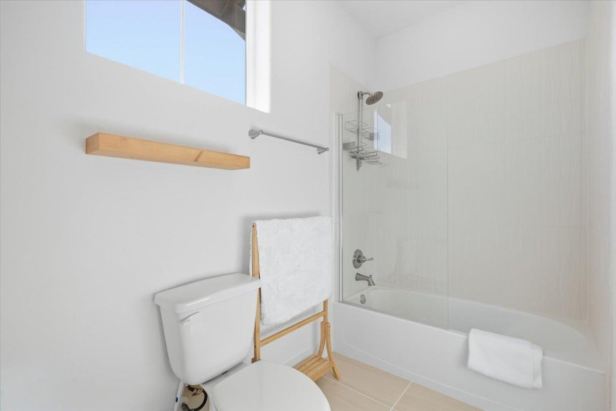 Bright bathroom with a white tub and glass shower panel beneath a high window.