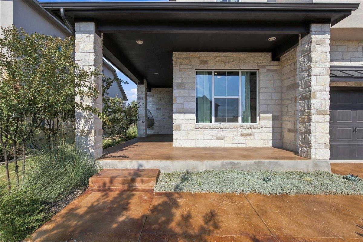 Stone home entry with a covered porch, broad window, and landscaped walkway.