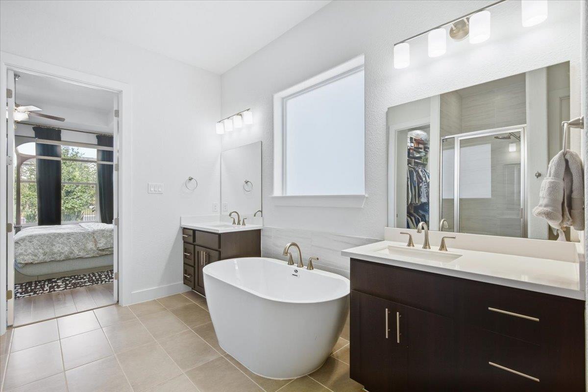 Primary bathroom with a freestanding tub and dark double vanity; bedroom visible through the doorway.